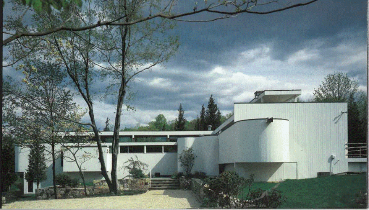 A white house with a tree and a cloudy sky
