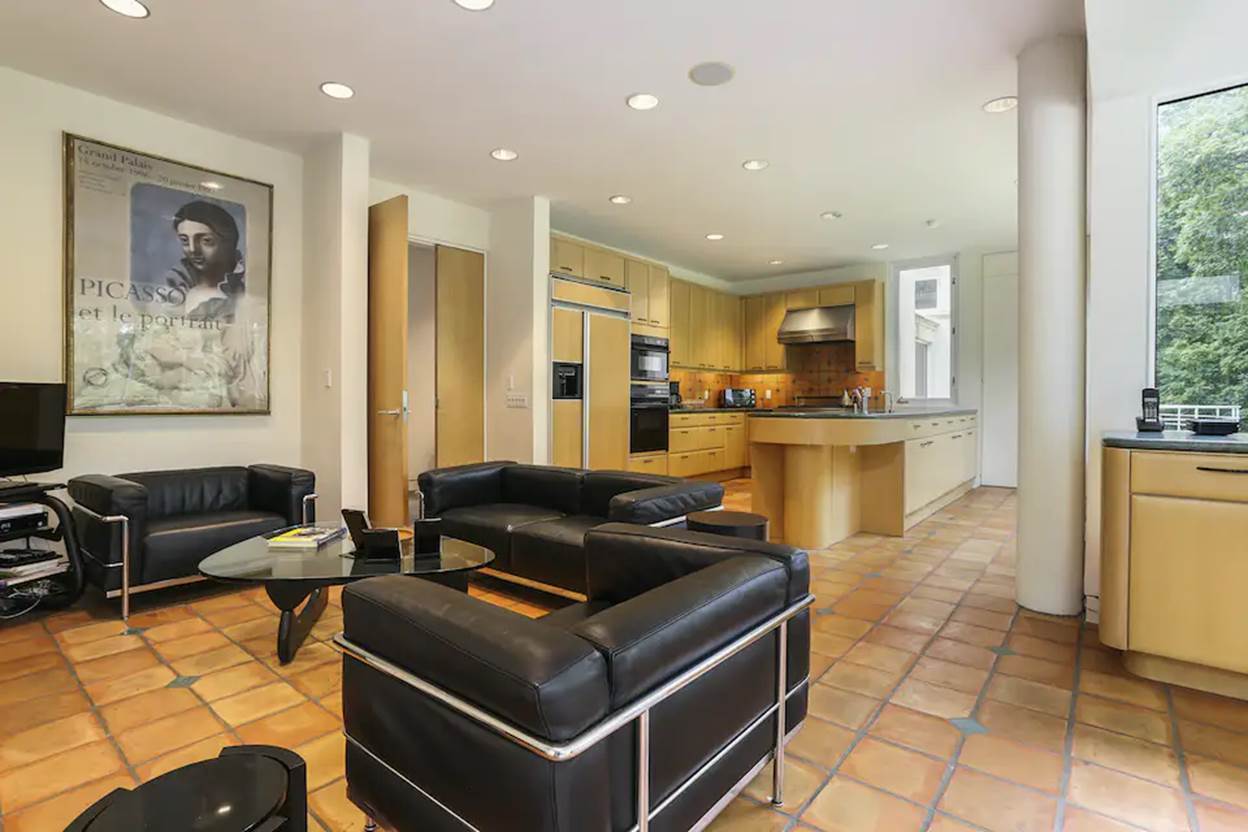 A living room with black leather couches and a kitchen
